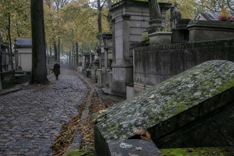 Una avenida empedrada y arbolada de tumbas desgastadas y piedra musgosa en el cementerio de Père Lachaise, en una mañana de noviembre brumosa, con entrada gratuita.